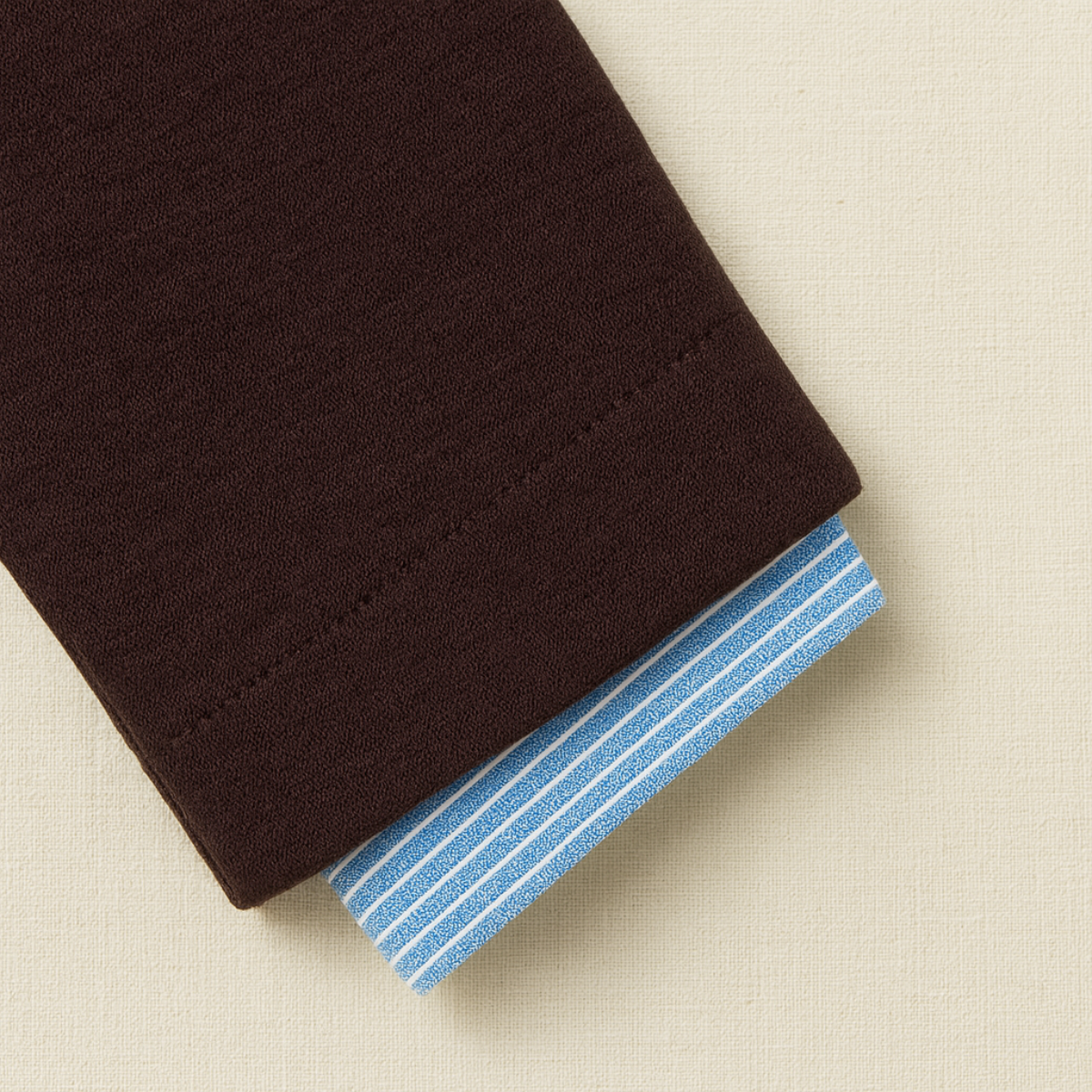 Close-up of a folded brown fabric with blue striped lining on a beige background