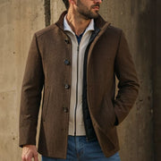 Man wearing a brown coat with a concrete wall background